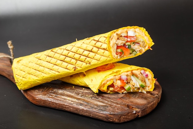 shawarma de queso en pan de pita amarillo con carne frita y verduras en una tabla vieja de corte de madera