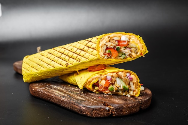 shawarma de queso en pan de pita amarillo con carne frita y verduras en una tabla vieja de corte de madera