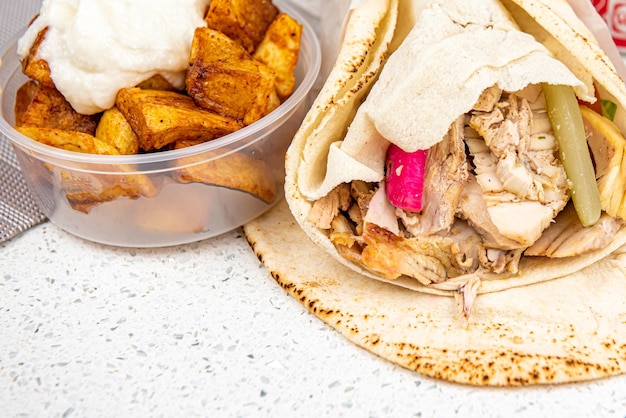 Shawarma-Sandwich-Rolle mit gegrilltem Hähnchen und Kartoffelecken mit weißer Soße auf weißem Tischhintergrund