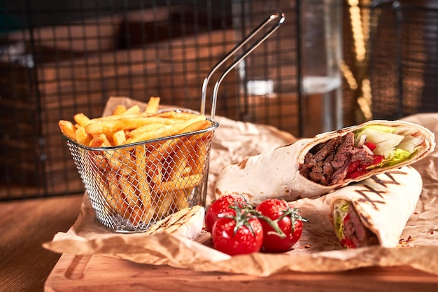 Foto shawarma turco con carne de res y frito con tomates en papel artesanal sobre plato de madera juego de comida rápida vista lateral