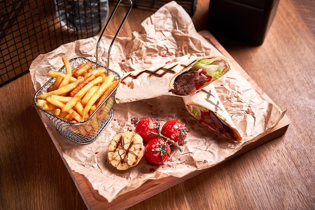 Foto shawarma turco com carne e frito com tomate em papel artesanal na placa de madeira conjunto de fast food vista lateral