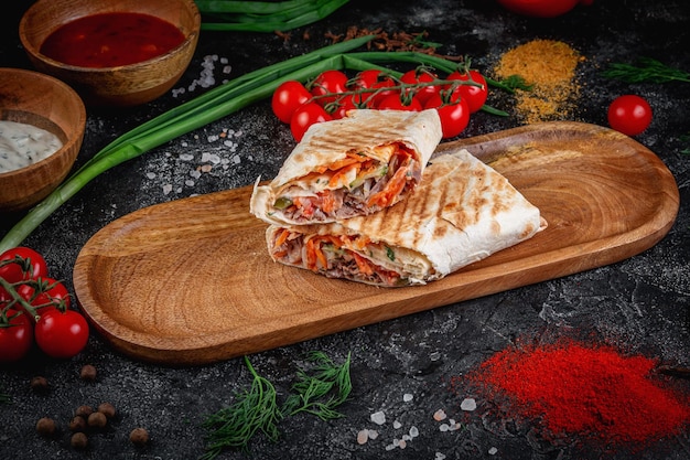 Shawarma con verduras en una tabla de madera con salsa de pita en una mesa de piedra oscura decorada con tomates cherry Servicio de entrega de restaurante de comida rápida