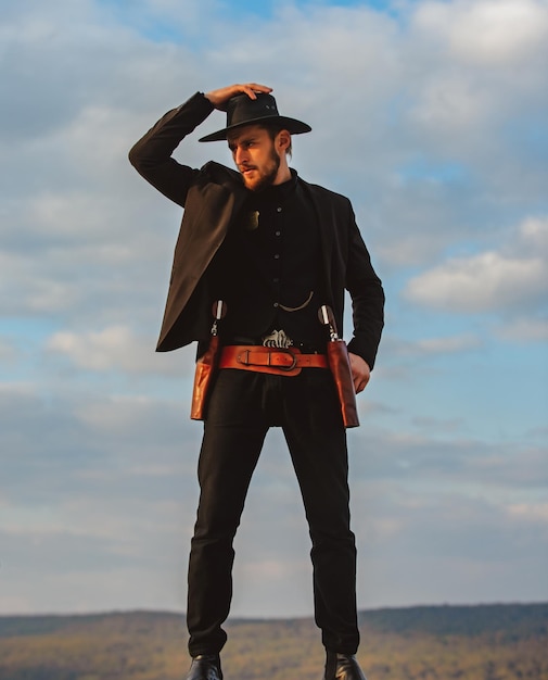 Foto sheriff o vaquero con traje negro y sombrero de vaquero hombre con revólver de pistola vintage del oeste y municiones de mariscal