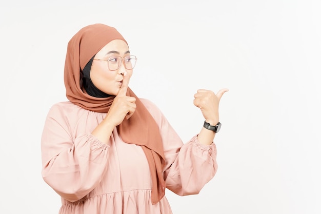 Shh Geste Präsentieren und Zeigen des Seitenprodukts mit dem Daumen einer schönen asiatischen Frau, die Hijab trägt