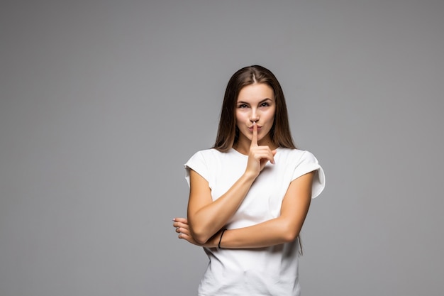 Shh. Mujer bonita joven mostrando gesto silencioso en gris