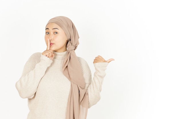 Shh und zeigt neben der schönen asiatischen Frau mit Hijab isoliert auf weißem Hintergrund