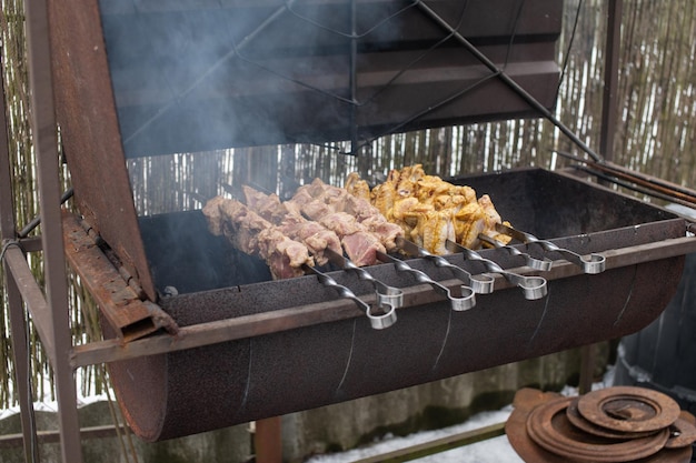 Shish kebab de diferentes tipos de carne em espetos são fritos na grelha de fumaça do fogo