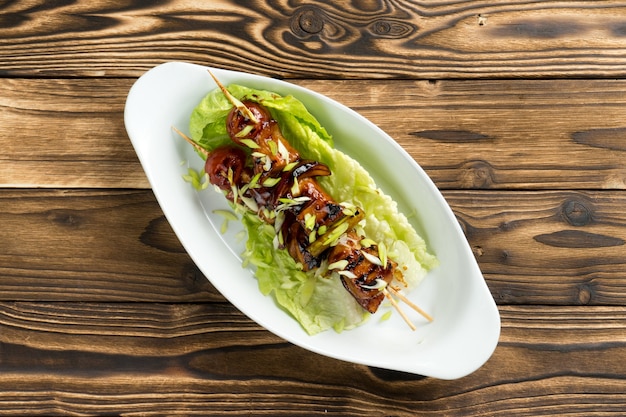 Shish kebab de frango e abobrinha em molho teriyaki com folhas de alface e cebolinha em um lindo prato de cerâmica na mesa da cozinha de madeira.