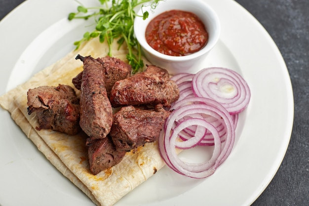 Shish kebab frito con lavash, salsa, microgreen y cebolla en un plato blanco sobre gris