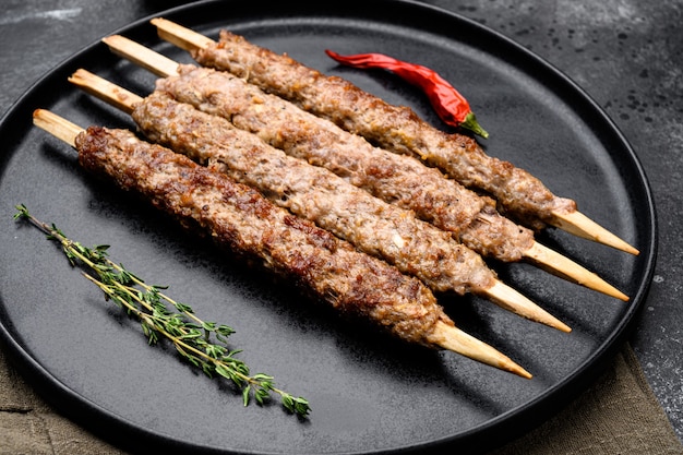 Shish kebab no palito, de carne de carneiro de terra moída definido, no prato, no fundo da mesa de pedra escura preta