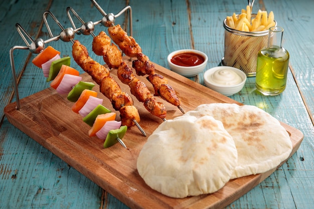 Shish tawook shashlik tikka boti kabab pão pita batatas fritas molho de maionese e molho de pimenta servido em uma vista lateral do prato isolado na mesa de madeira