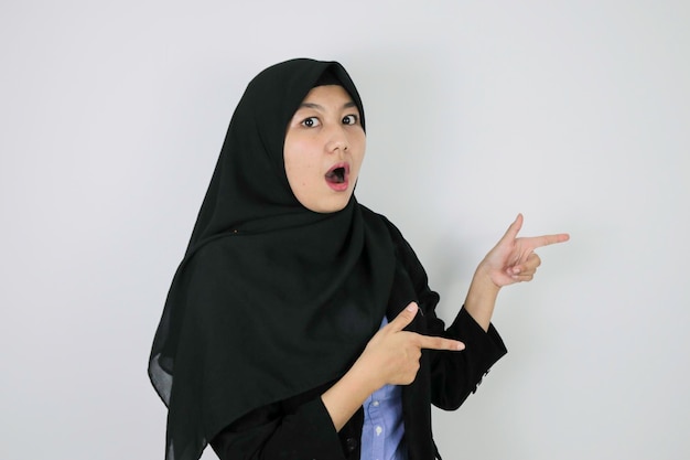 Shock Young Asian Islam mujer con pañuelo en la cabeza sonríe y señala al lado