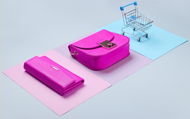 Shopaholic minimalistisches Konzept. Tasche, Geldbörse, Mini-Einkaufswagen auf Pastellhintergrund. Seitenansicht