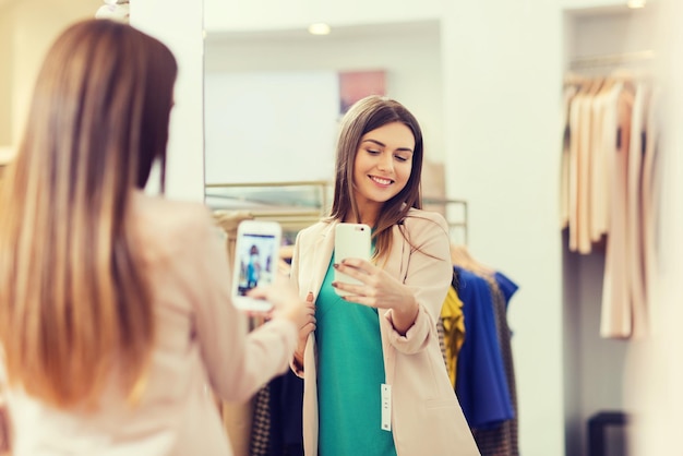 Shopping-, Mode-, Stil-, Technologie- und People-Konzept – glückliche Frau mit Smartphone macht Spiegel-Selfie im Bekleidungsgeschäft