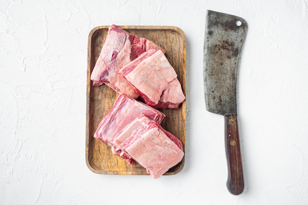 Short Ribs Bone In Eintopfset und altem Fleischbeilmesser auf weißem Steinhintergrund, Draufsicht flach legen, mit Kopierraum für Text