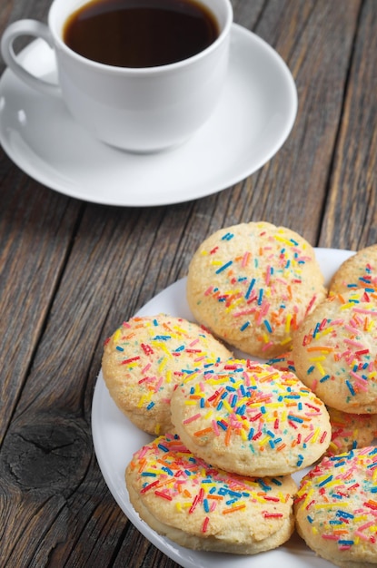 Shortbread Cookies mit farbigen Streuseln und Tasse Kaffee auf altem Holztisch hautnah