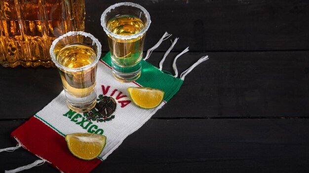 Shots de tequila mexicanos acompanhados por uma garrafa quadrada de luxo em uma mesa de madeira com limões