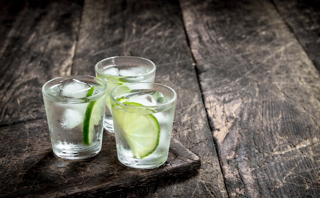 Shots de vodka com limão e gelo no quadro. Sobre um fundo de madeira.