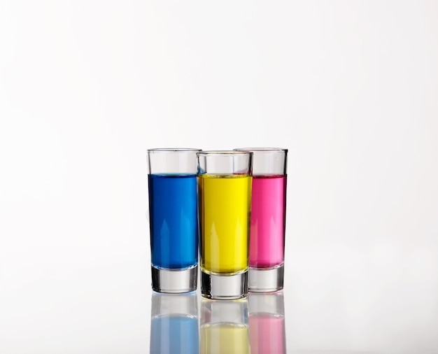 Shots - três bebidas shot coloridas em branco com reflexos