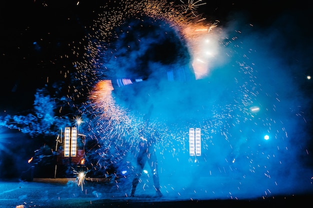 Show de fogo, dançando com chamas, mestre masculino fazendo malabarismo com fogos de artifício, performance ao ar livre, desenha uma figura de fogo no escuro, faíscas brilhantes à noite. Um homem em um terno LED dança com fogo.