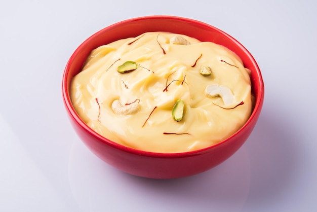 Shrikhand es un plato dulce indio hecho de yogur colado, aderezado con frutos secos y azafrán. Servido en cuenco de cerámica. Aislado sobre fondo de colores o madera. Enfoque selectivo