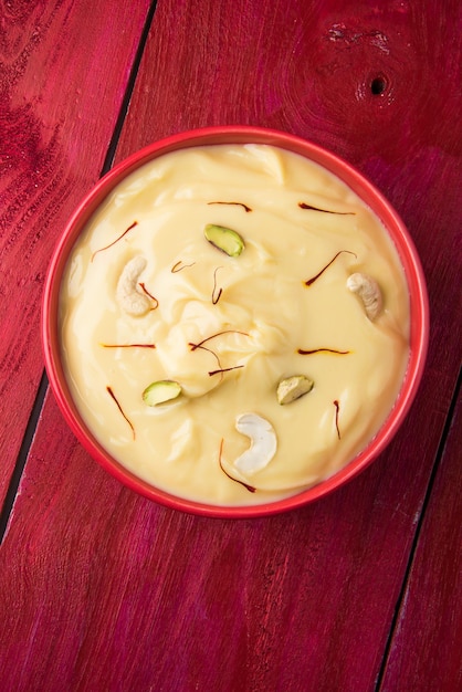 Shrikhand ist eine indische Süßspeise aus passiertem Joghurt, garniert mit Trockenfrüchten und Safran. Serviert in einer Keramikschale. Getrennt über buntem oder hölzernem Hintergrund. Selektiver Fokus