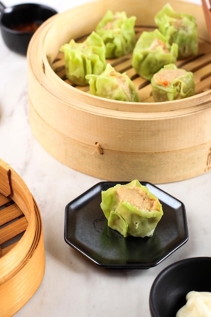 Shumai de verduras con color de piel verde, bola de masa de Dim Sum al vapor en un vaporizador de bambú