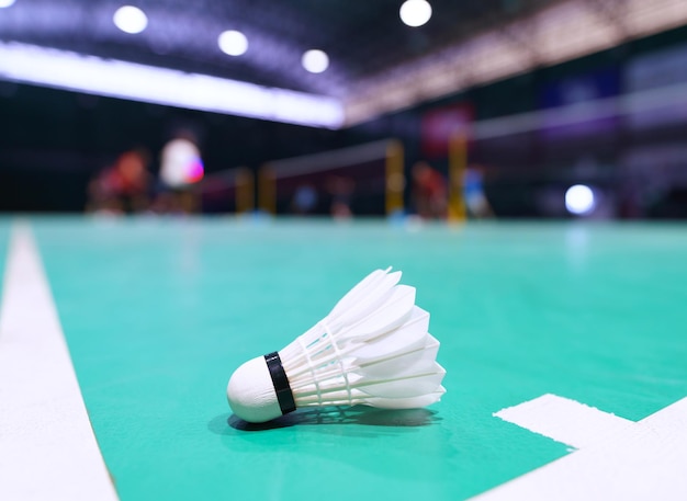 Shuttlecock en cancha de bádminton verde con jugador en segundo plano.