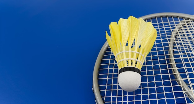 Shuttlecock de pluma amarela de badminton em uma raquete de badmington sobre uma imagem de tamanho de bandeira de fundo azul