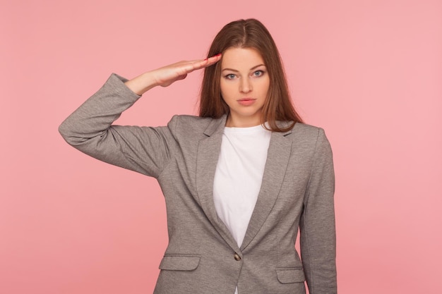 Sí, señor Retrato de una joven seria e inteligente con traje de negocios que saluda escuchando atentamente el pedido mirando con una expresión atenta y responsable en un estudio aislado en un fondo rosa