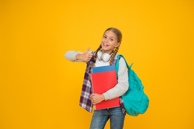 Si te gusta dale pulgar arriba. Niño feliz gesticulando pulgares arriba fondo amarillo. La pequeña colegiala muestra el pulgar hacia arriba. El niño pequeño sonríe con los pulgares hacia arriba. Escuela y educación.