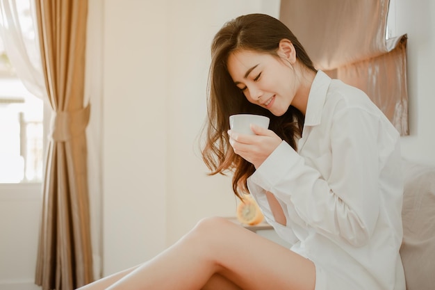 Ásia jovem vivendo em casa, relaxando e bebendo café quente no quarto de férias. Asiático, ásia, relaxe, sozinho, tecnologia, conceito de estilo de vida.