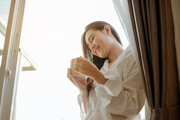 Ásia jovem vivendo em casa, relaxando e bebendo café quente no quarto de férias. Asiático, ásia, relaxe, sozinho, tecnologia, conceito de estilo de vida.