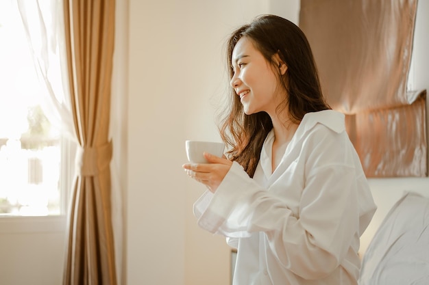 Ásia jovem vivendo em casa, relaxando e bebendo café quente no quarto de férias. Asiático, ásia, relaxe, sozinho, tecnologia, conceito de estilo de vida.