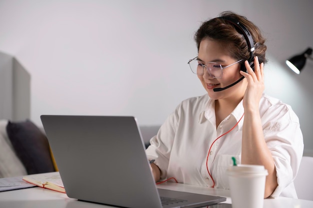 Foto sich bei der arbeit wohl und positiv fühlen. junge asiatische geschäftsfrau mit headset bei videoanruf mit kunden am laptop. junge asiatische frau, die online-vorlesung im bildungsunterricht hält und kunden berät.