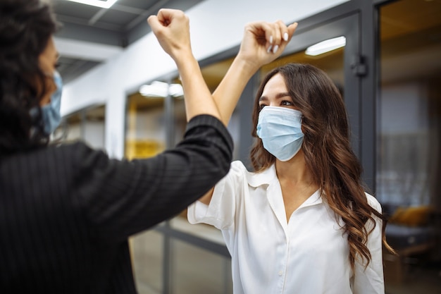 Sichere Begrüßung von zwei Geschäftsfrauen, die während der Coronavirus-Pandemie Masken tragen.