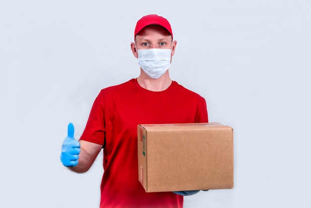 Sichere Lieferung. Kurier in roter Uniform und medizinischer Schutzmaske und Handschuhen hält einen Karton, kontaktlose Lieferung von Bestellungen. Spende von Freiwilligen.