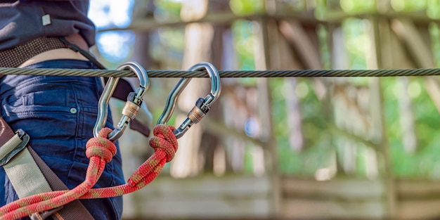 Sicherheitsausrüstung im Walderlebnispark. Die Verwendung von Ausrüstung zum Bergsteigen: Karabiner, Gürtel, Seil. Banner für Werbung, Design oder Website-Header.