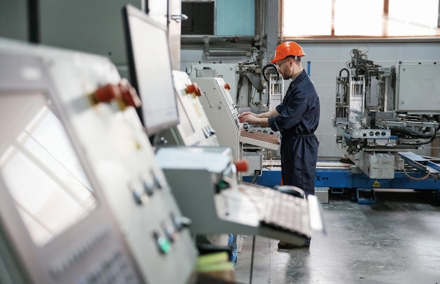 Foto sicht von der seite bei der arbeit mit dem maschinenbediener fabrikarbeiter ist im innenraum mit hut