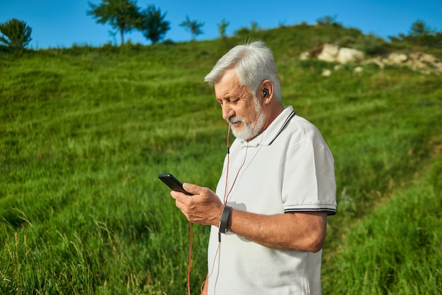 Sideview des alten Mannes draußen schauend auf seinem Mobiltelefon.