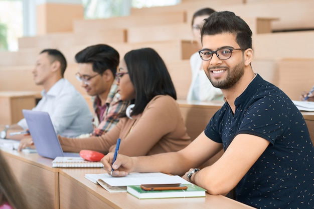 Sideview des arabischen Studenten sitzend in der Universität und in Kamera betrachtend.