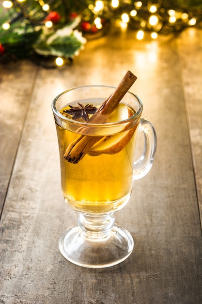 Sidra caliente en adornos de vidrio y luz de navidad en mesa de madera