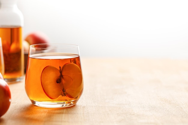 Sidra de suco de maçã caseiro fresco em um copo e maçãs frescas na mesa de madeira