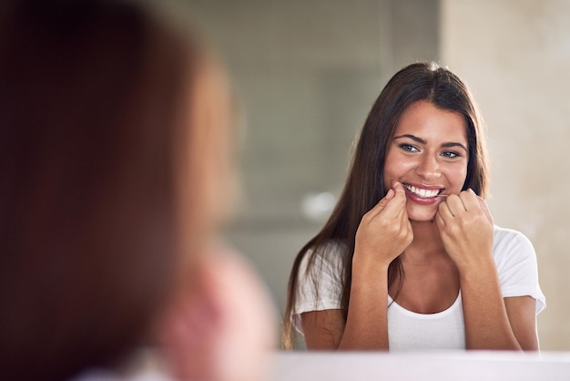 Sie hört immer auf ihren Zahnarzt Aufnahme einer schönen Frau, die ihre Zähne mit Zahnseide behandelt, während sie in den Spiegel schaut