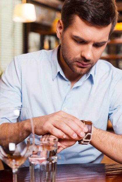 Sie ist wieder zu spät. Frustrierter junger Mann, der die Zeit überprüft, während er im Restaurant sitzt?