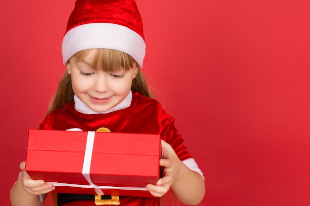 Foto sie liebt geschenke. studioporträt eines kleinen mädchens, das weihnachtsmütze und weihnachtsmann-outfit trägt, das ein geschenk prüft, das es in ihren händen hält, die fröhlich lächeln