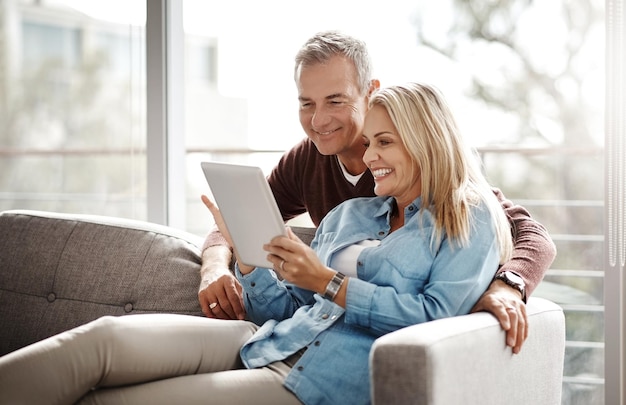 Sie machen Bildschirmzeit als Paar Aufnahme eines älteren Paares, das ein digitales Tablet verwendet, während es sich zu Hause auf dem Sofa entspannt