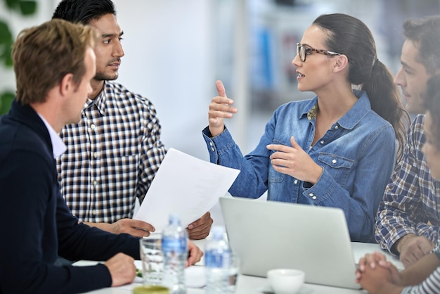 Sie präsentiert ihre Ideen gut Selbstbewusste Geschäftsfrau, die ihren Kollegen bei einem Meeting eine Idee erklärt