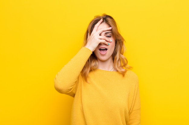 Sie sehen schockiert, verängstigt oder verängstigt aus, bedecken das Gesicht mit der Hand und spähen zwischen den Fingern