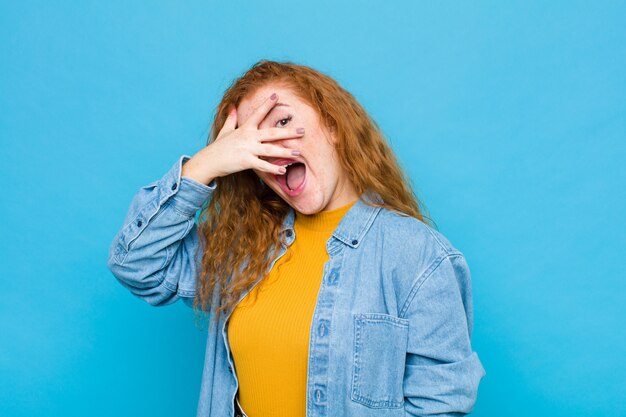 Sie sehen schockiert, verängstigt oder verängstigt aus, bedecken das Gesicht mit der Hand und spähen zwischen den Fingern